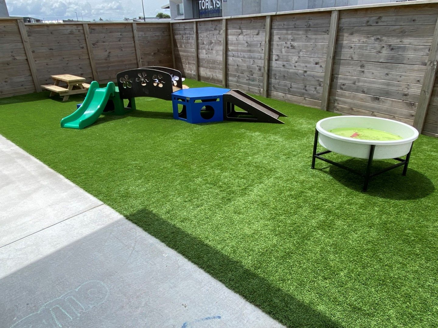 Nurture and Bloom | Outdoor playspace with artificial grass, slides, bridge and climbing equipment