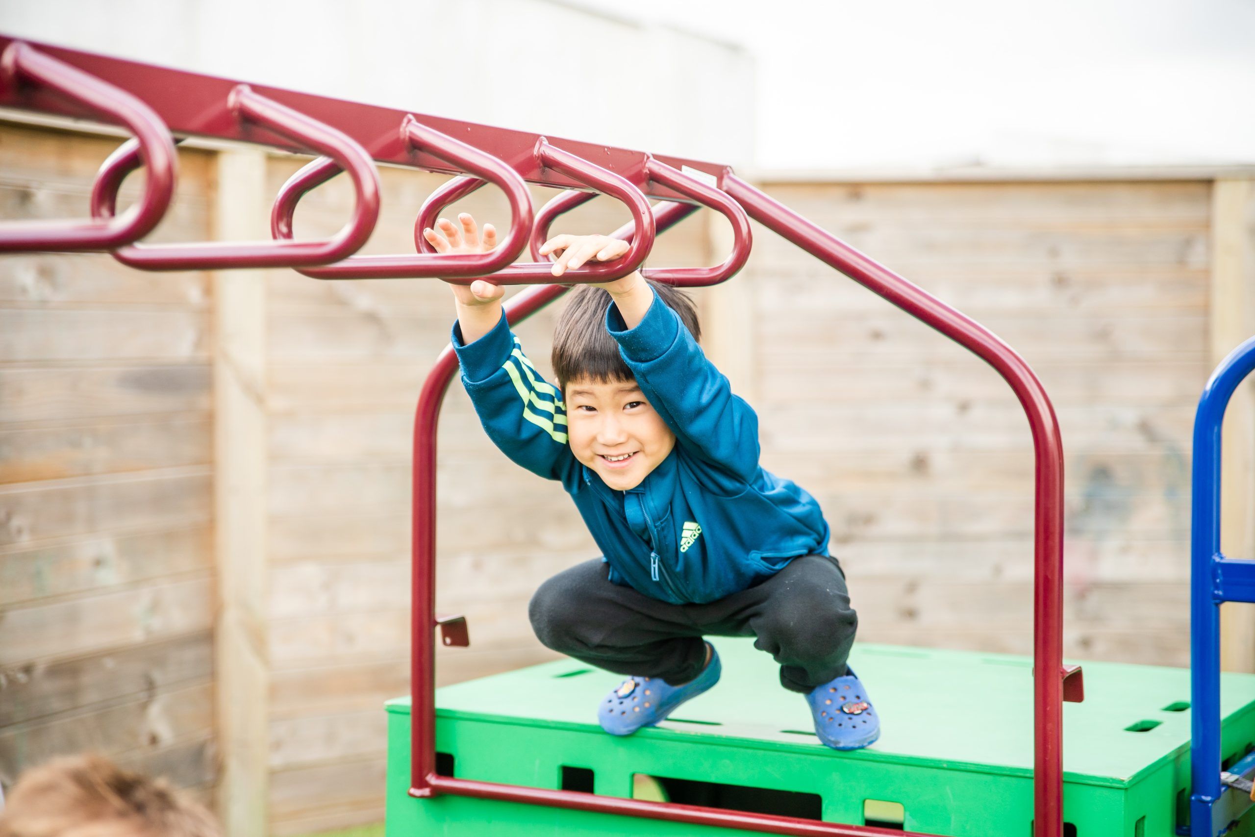 Nurture and Bloom | Child on outdoor play equipment; monkey bars