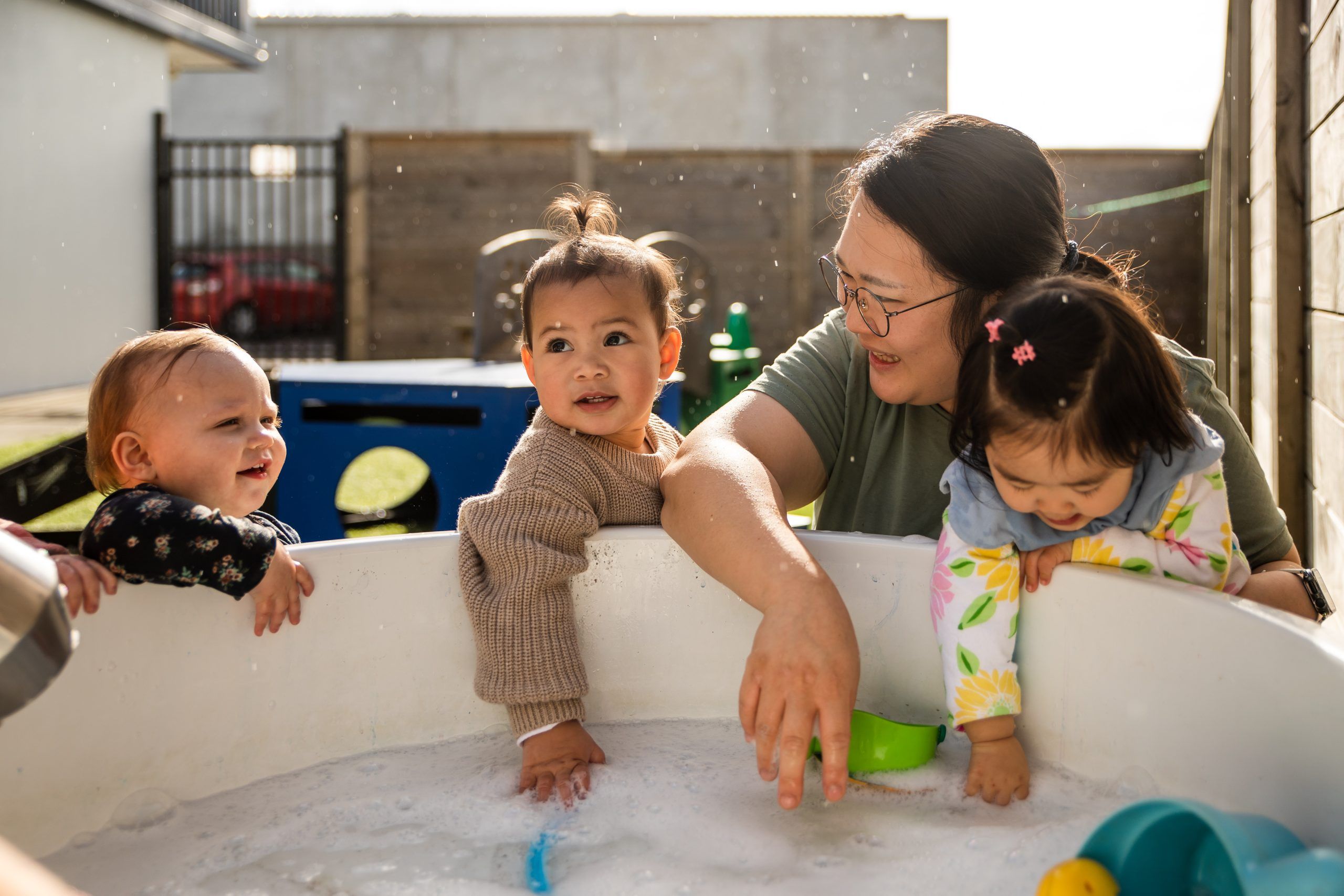 Nurture & Bloom | Children playing outdoors with water play in tub